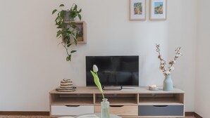 A modern living room with a flat-screen TV, a bookshelf, a small table with a candle, and a vase with dried flowers. - Nonna Tere Apartment (Carate Urio)