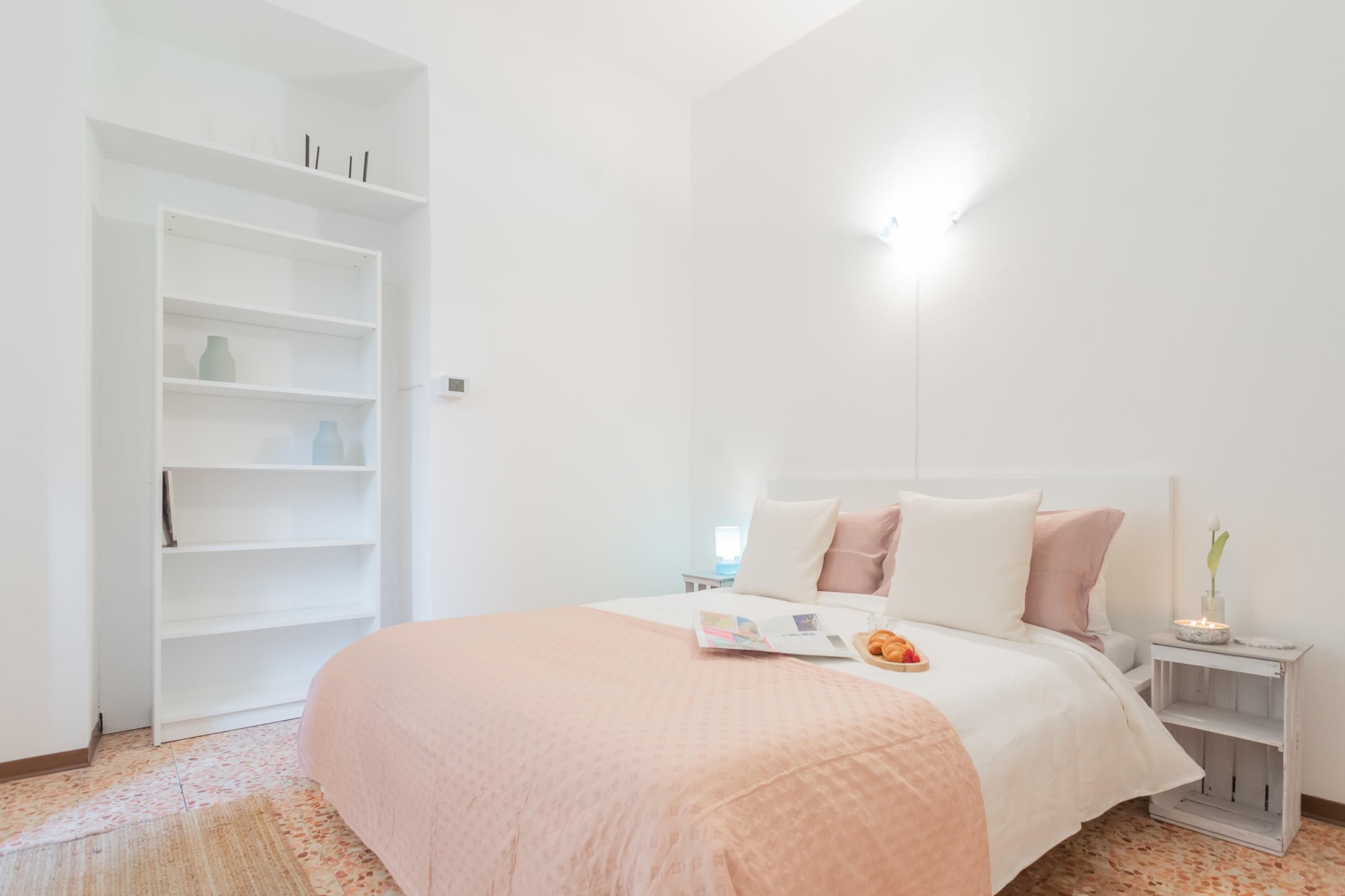 A bedroom with a bed, bedside tables, a nightstand, and a white wardrobe.