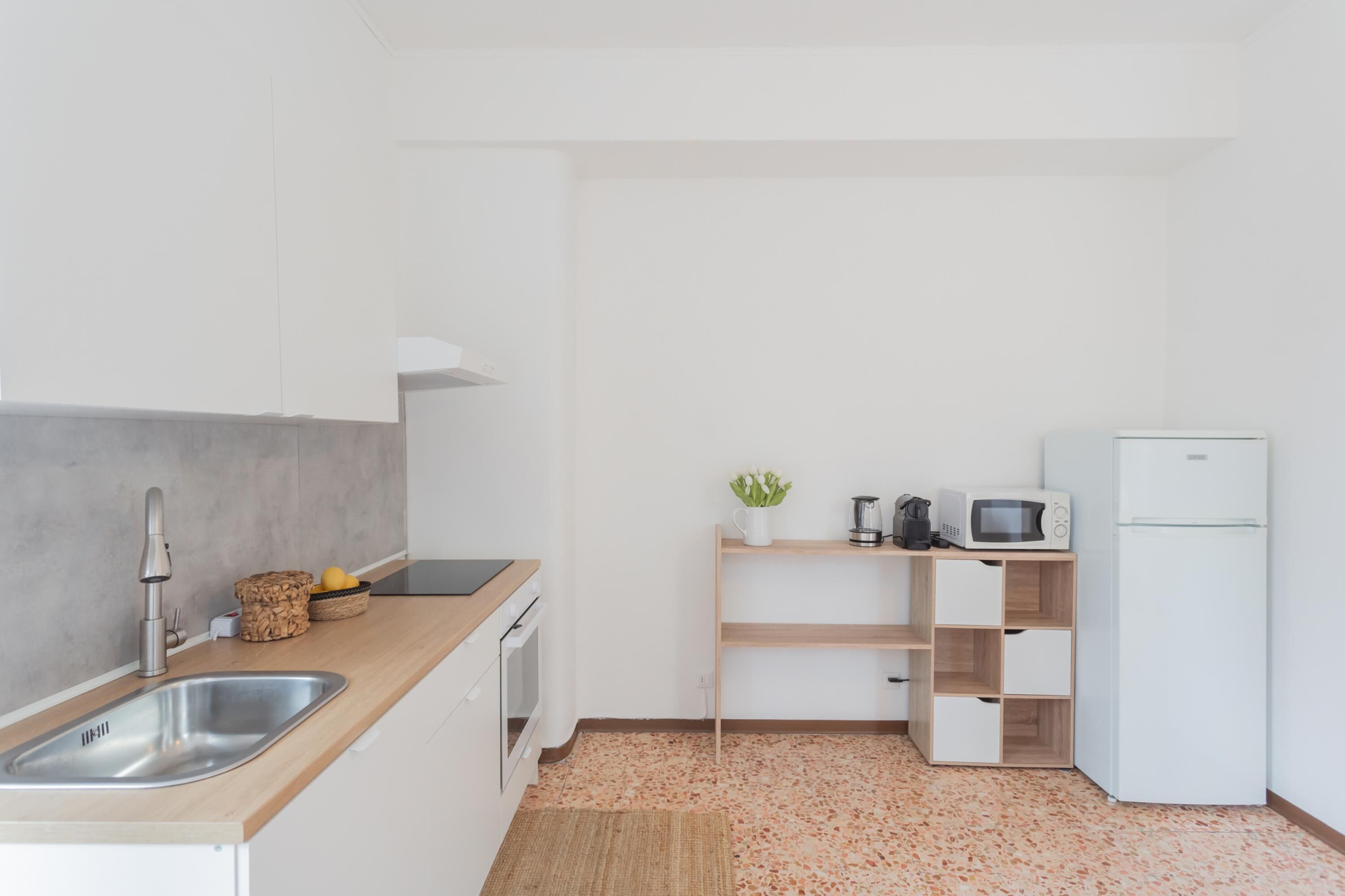 A modern kitchen with a stainless steel sink, wooden countertop, white cabinets, a microwave, a refrigerator, and a small plant on a shelf.