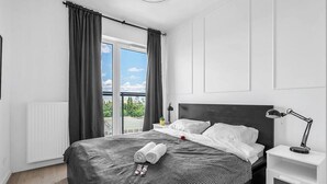Une chambre moderne avec un grand lit, une table de chevet, une lampe et une vue sur la verdure.