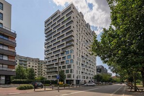 A modern high-rise building with multiple balconies, a parking area, and a clear sky. - Rondo Daszyńskiego Apt N3 - 8th Floor, Near Subway by Rentujemy (Warszawa)