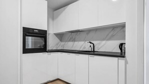 Une cuisine compacte avec des meubles blancs, un plan de travail noir, un four encastré et une machine à café.