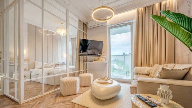 Ein modernes Wohnzimmer mit großem Fernseher, bequemen Sitzmöglichkeiten, einem runden Couchtisch und Blick ins Freie.