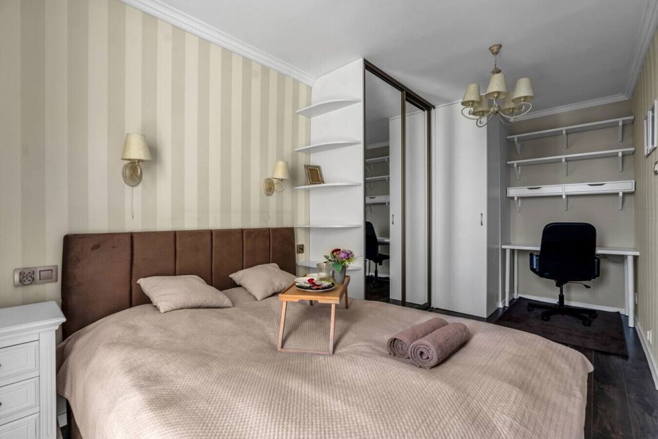 Un dormitorio ordenado con una cama grande, mesitas de noche, un escritorio y una silla.