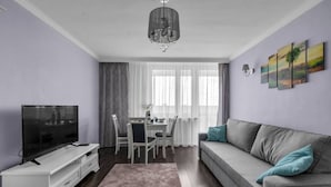 A living room with a TV, sofa, and dining table. - Warsaw Praga View - 17th Floor with Balcony - by Rentujemy (Warszawa)