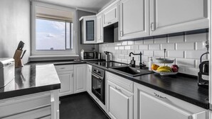 A modern kitchen with white cabinets, a black countertop, a built-in microwave, and a sink. - Warsaw Praga View - 17th Floor with Balcony - by Rentujemy (Warszawa)