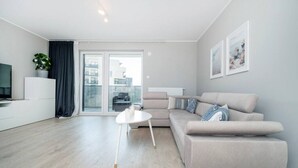 En moderne stue med sofa, et lille hvidt bord og et fjernsyn på et hvidt skab.