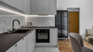 Una cocina moderna con encimera negra, armarios blancos, horno integrado y campana extractora de acero inoxidable.