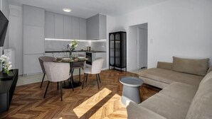 Una sala moderna con un sofá, una mesa de comedor con sillas, un mueble negro y un suelo de madera con patrón de espiga.