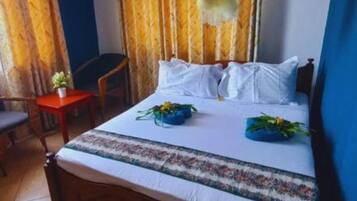 A bedroom with a bed, a small table with a plant, a chair, and a ceiling fan.