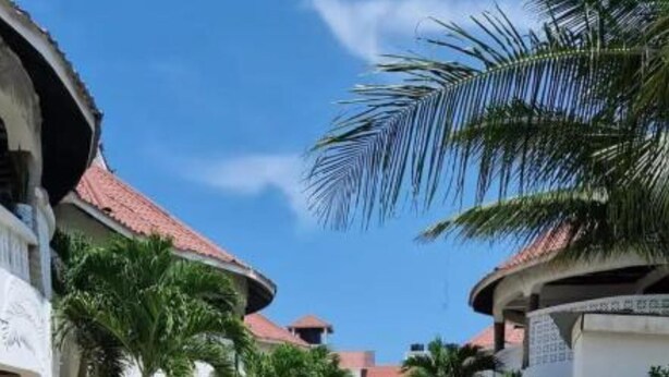 A paved courtyard with palm trees and buildings with red-tiled roofs. - Casa Villa Diani (Diani Beach)