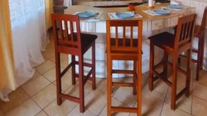 A dining area with a wooden table and chairs, a kitchen in the background, and a tiled floor. - Casa Villa Diani (Diani Beach)