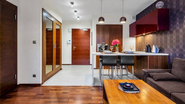 A modern living room with a wooden floor, a sofa, a coffee table, and a kitchen area with a dining table and chairs.