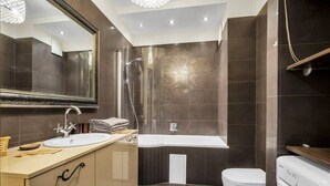 A modern bathroom with a large mirror, a sink, a shower, a toilet, and a washing machine.