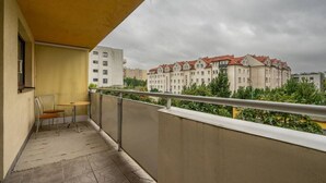 Un balcon avec une chaise et une table, donnant sur une rangée d’immeubles aux toits rouges.