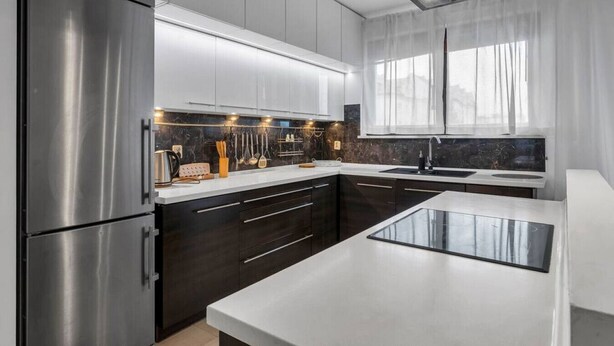 Une cuisine moderne dotée d’appareils électroménagers en acier inoxydable, de meubles de rangement aux couleurs sombres et d  ’un grand îlot central.