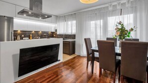 Une cuisine moderne dotée d’une cuisinière intégrée, d’un coin repas avec une table et des chaises, et d’une grande fenêtre ornée de rideaux légers.