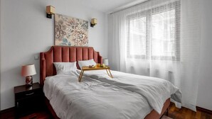Un lit bien fait, avec un plateau en bois, du linge de lit blanc et une tête de lit rouge.