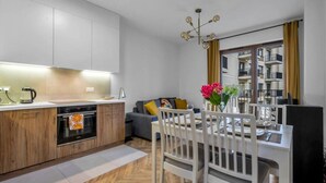 A modern kitchen with wooden cabinets, a built-in oven, and a dining area with a white table and chairs. - Business District Apartment - Parking, Balcony by Rentujemy (Warszawa)