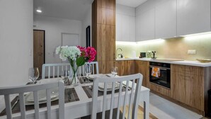 A modern kitchen with white cabinetry, a wooden accent wall, and a dining area with a white table and chairs. - Business District Apartment - Parking, Balcony by Rentujemy (Warszawa)