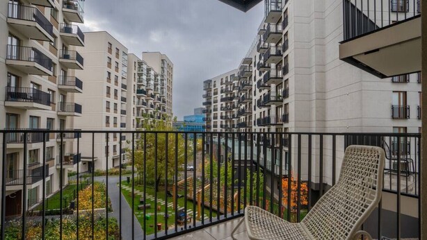 A balcony with a chair, overlooking a residential area with multiple apartment buildings and a green park. - Business District Apartment - Parking, Balcony by Rentujemy (Warszawa)