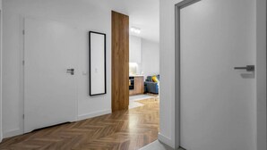 A hallway with a wooden floor, white walls, and a door leading to a room with a kitchen area. - Business District Apartment - Parking, Balcony by Rentujemy (Warszawa)