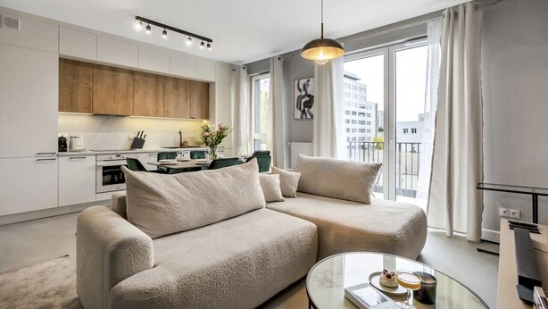 Ein modernes Wohnzimmer mit einem beigefarbenen Sofa, einem Glastisch und Blick auf die Stadt durch große Fenster.