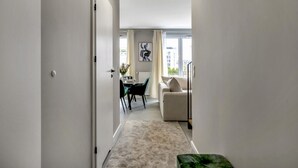 Ein schmaler Flur führt zu einem Essbereich mit Tisch und Stühlen, einer Couch und einem Fenster mit Vorhängen.