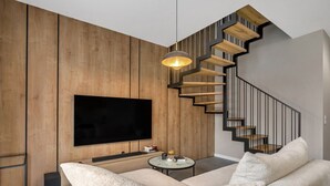 Ein modernes Wohnzimmer mit einem großen Flachbildfernseher, einem runden Couchtisch und einem beigen Sofa.