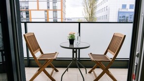 En balkong med två trästolar och ett litet bord, en krukväxt och en vattenflaska.