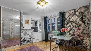 Een knus woongedeelte met een kitchenette, een eethoek met tafel en stoelen, een grote spiegel en bloemenbehang.