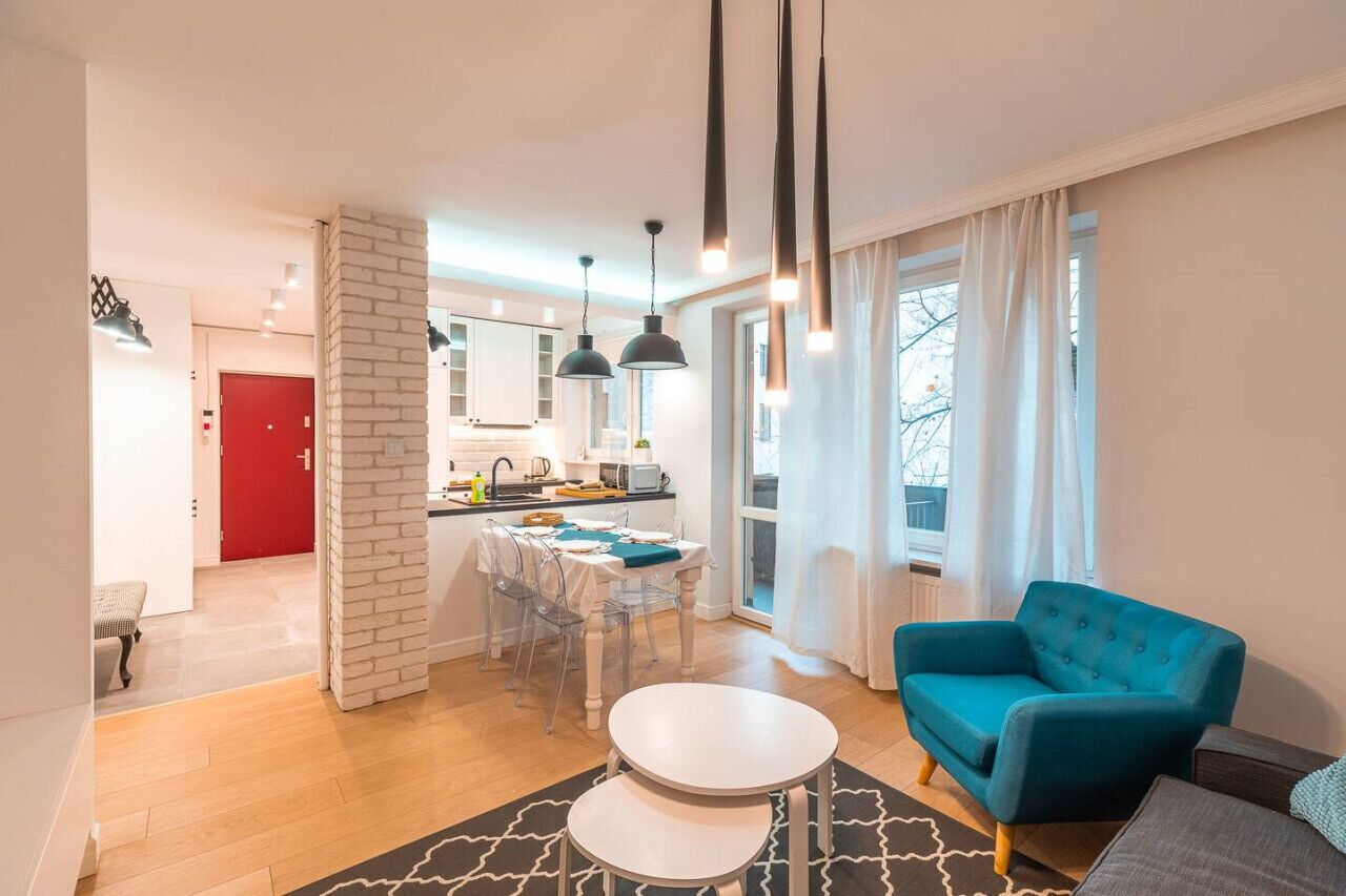 Een moderne woonkamer met een blauwe bank, een eethoek met een witte tafel, en een keuken op de achtergrond.