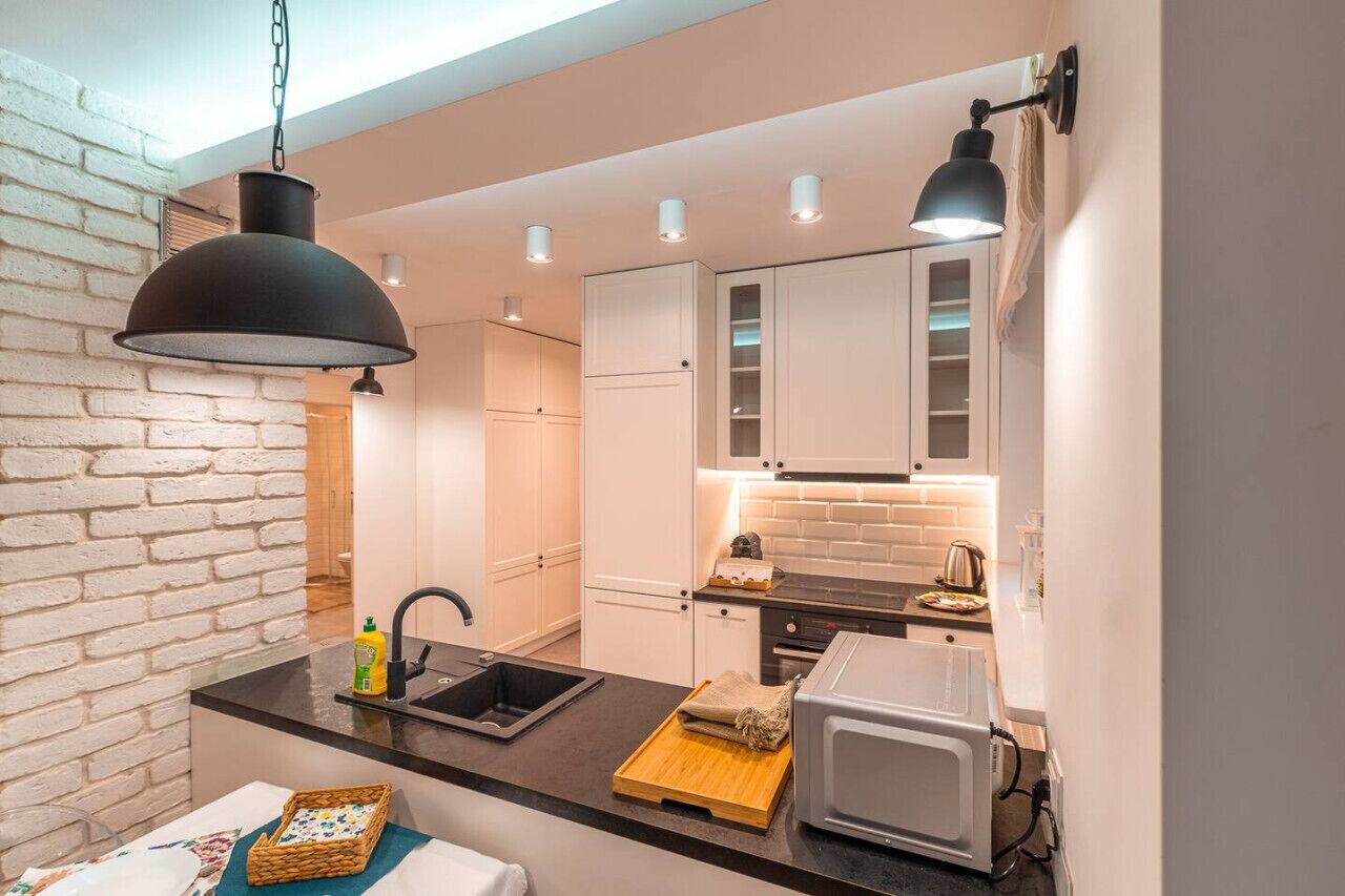 A compact kitchen with a black pendant light, white cabinets, a microwave, and a sink.