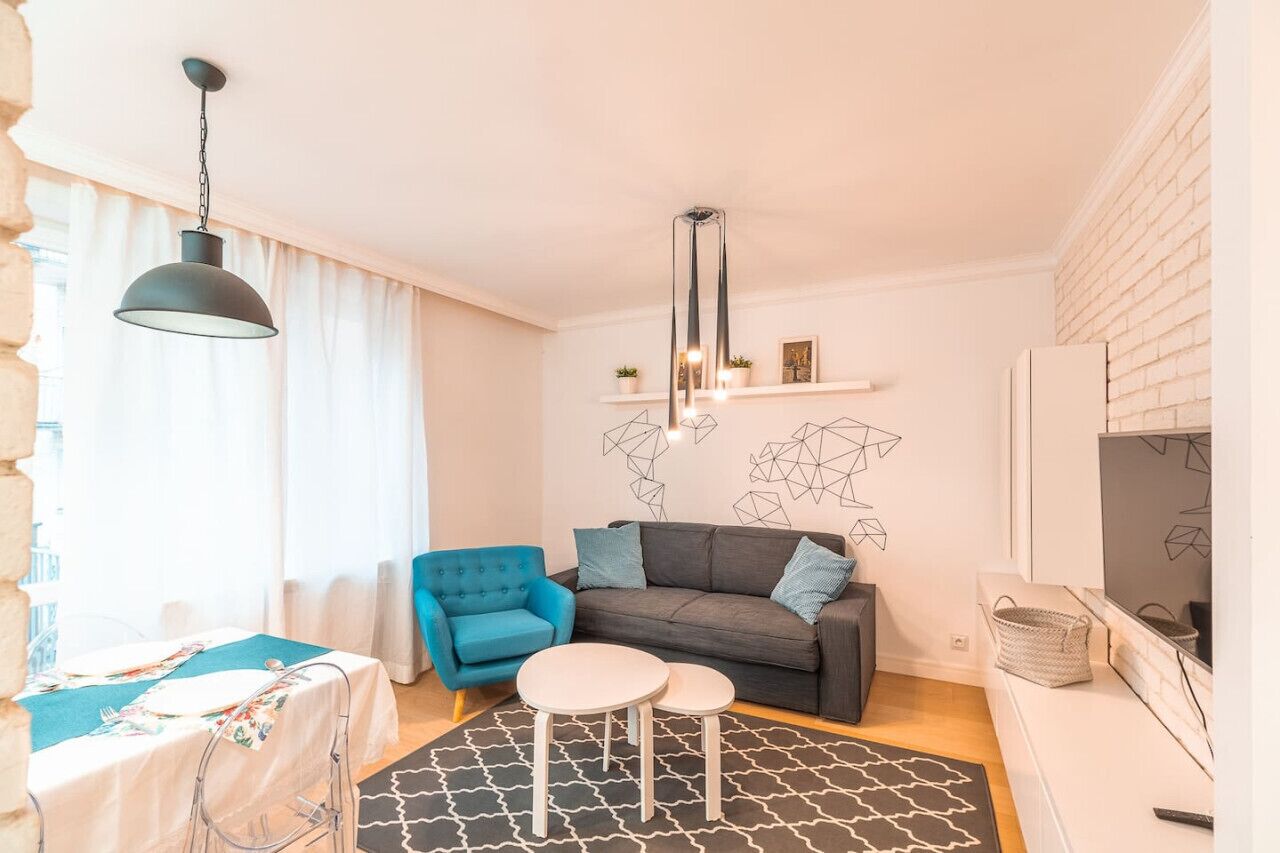 Een moderne woonkamer met een bank, een blauwe fauteuil, een eettafel en een zwart-wit tapijt.