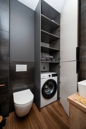 Ein kleiner Waschraum mit Waschmaschine, Toilette und fest installierten Regalen.