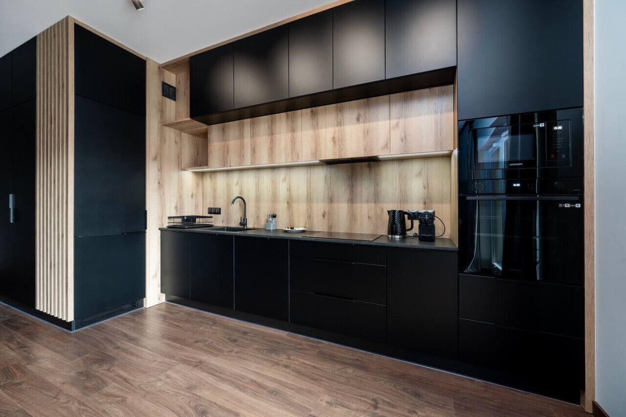 Una cocina moderna con armarios negros, una pared de acento de madera y electrodomésticos integrados.