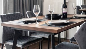 Un comedor moderno con una mesa rectangular, sillas grises tapizadas, una botella de vino y copas de vino vacías.