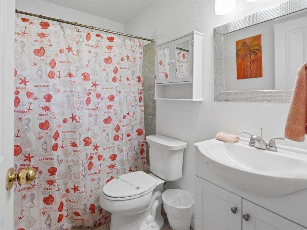A bathroom with a toilet, sink, and a shower curtain with nautical patterns.