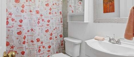 A bathroom with a toilet, sink, and a shower curtain with nautical patterns.