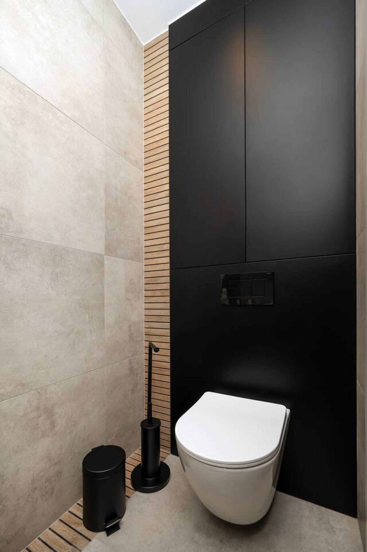 Un baño moderno con inodoro blanco, un cubo de basura negro y un escobillón negro.