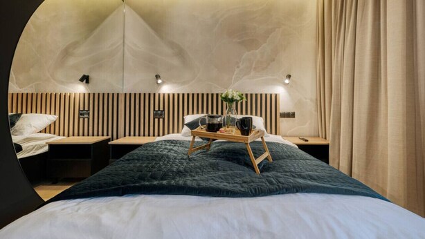 Habitació d'hotel moderna amb un llit gran, una taula de nit i un mirall fixat a la paret.