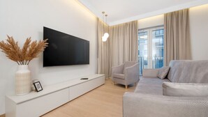 Un saló modern amb un televisor de pantalla plana muntat sobre una consola blanca, un sofà gris i una làmpada de peu alta.