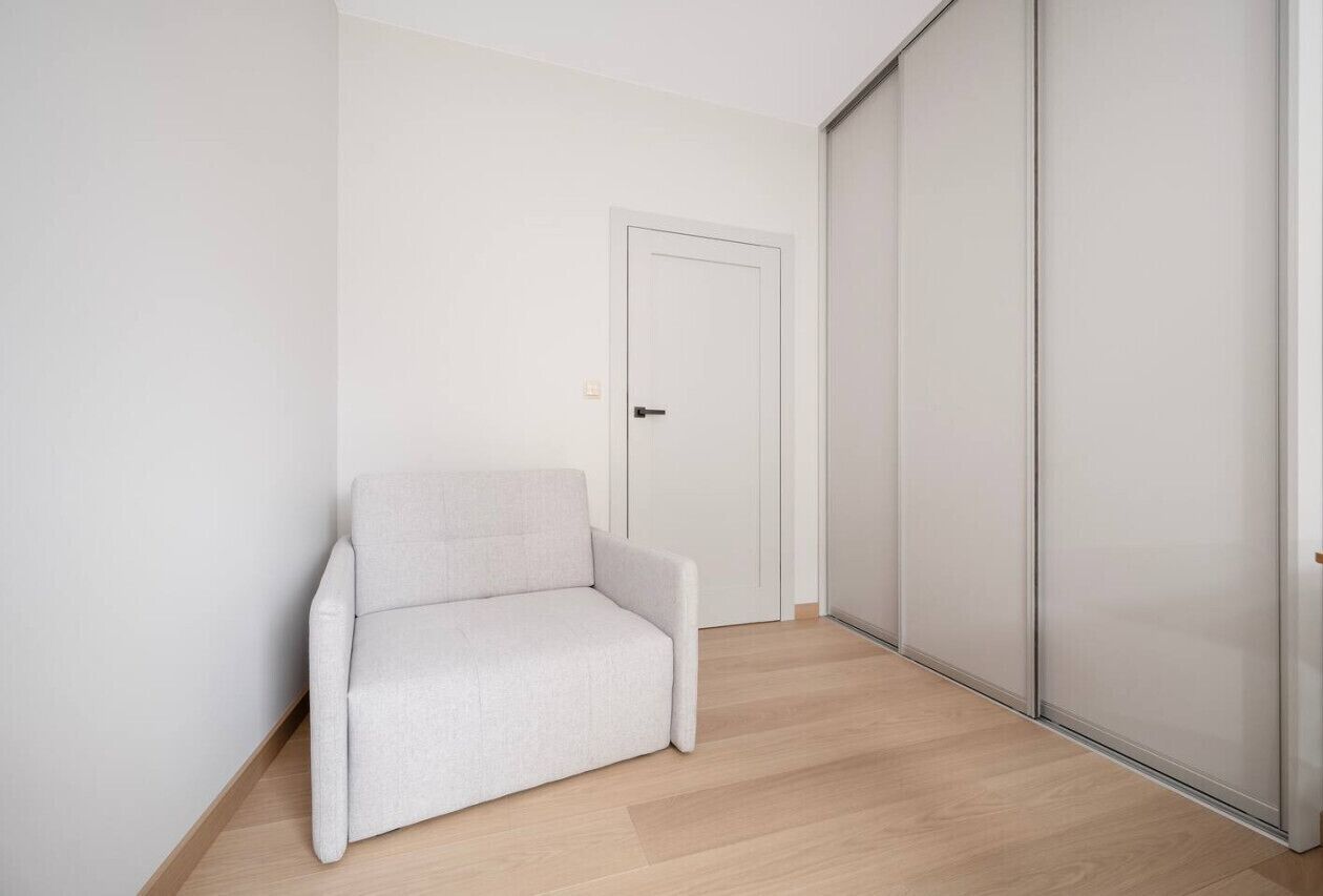 A room with a light-colored sofa, a white door, and a sliding closet door.