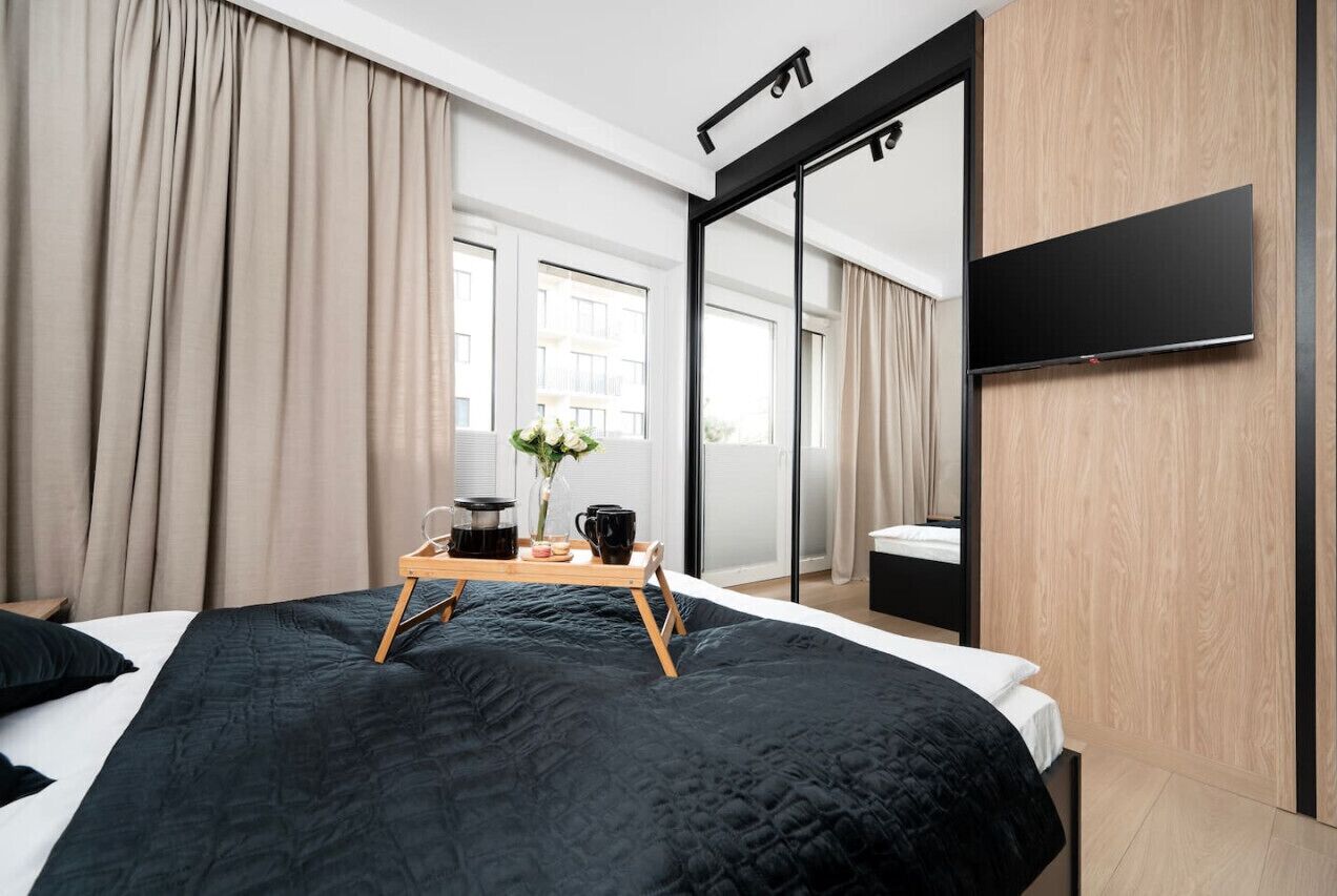Ein modernes Hotelzimmer mit einem großen Bett, einem Nachttisch mit Frühstücksgebäck und -zutaten, einem großen Spiegel und einem an der Wand befestigten Flachbildfernseher.