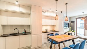 Una cocina moderna con armarios blancos, encimera negra y mesa de comedor de madera con sillas azules.