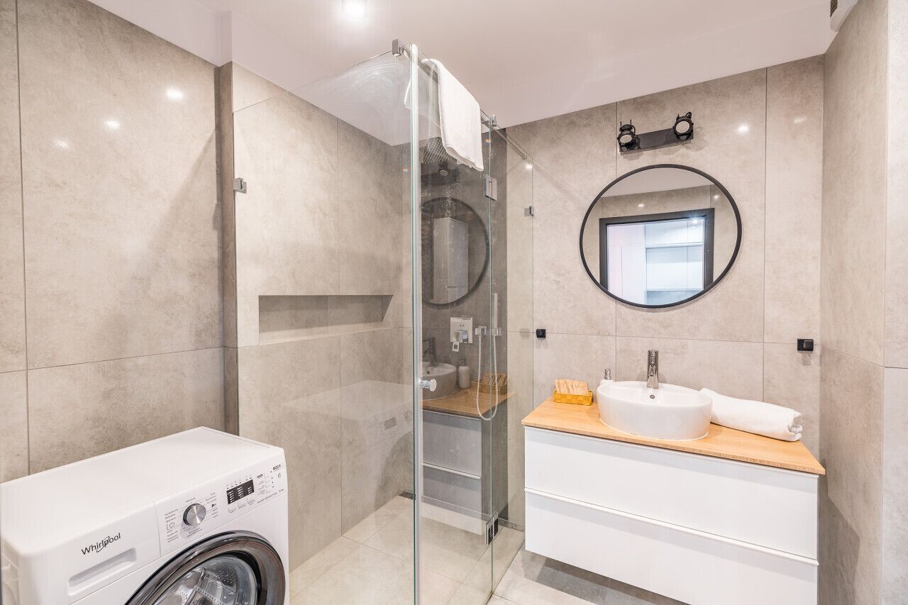 A modern bathroom with a glass-enclosed shower, a built-in sink, and a Whirlpool washing machine.