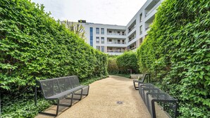 A pathway flanked by lush green hedges leading to a building with multiple balconies. - Warsaw Wola - Parking & Balcony - by Rentujemy (Warszawa)