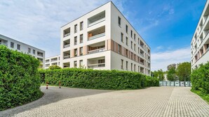 A modern multi-story building with balconies, a paved courtyard, and a hedge. - Warsaw Wola - Parking & Balcony - by Rentujemy (Warszawa)