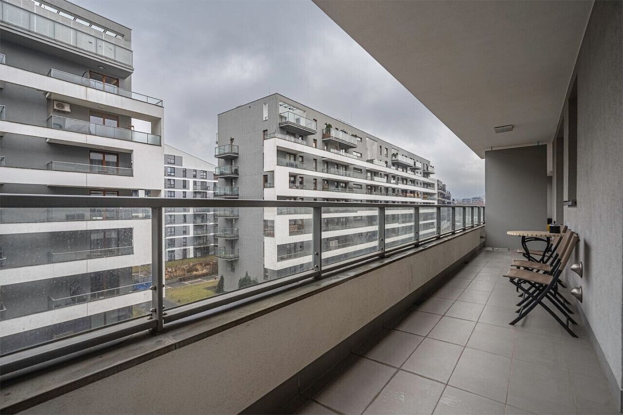 A balcony with a view of a multi-story building, a tiled floor, and a table with chairs.