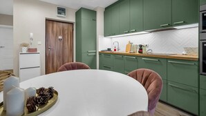 A modern kitchen with green cabinets, a white countertop, and a round dining table with chairs.